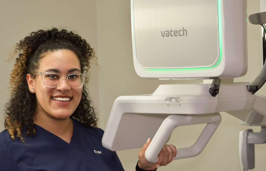 PHOTO OF CLINICAL STAFF WOMAN STANDING WITH HAND ON VATECH DIGITAL IMAGING MACHINE